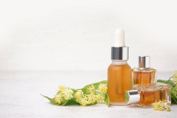 Bottles of essential oil and fresh linden flowers on light background