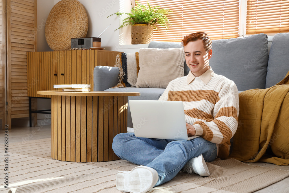 Poster redhead young happy man with laptop sitting on floor at home