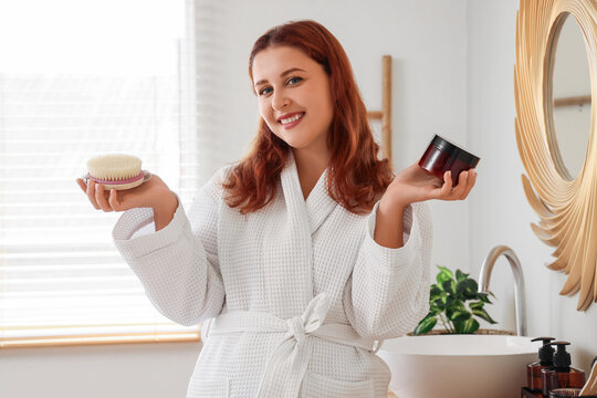 Beautiful plus size woman with anti-cellulite scrub and massage brush in bathroom - Powered by Adobe