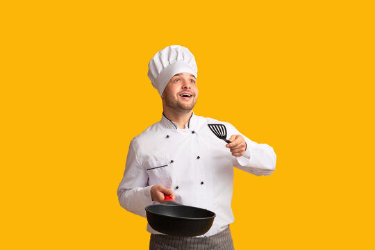 Excited Chef Cook Guy Holding Pan Throwing Invisible Food Looking Up Standing Over Yellow Background. Studio Shot, Empty Space