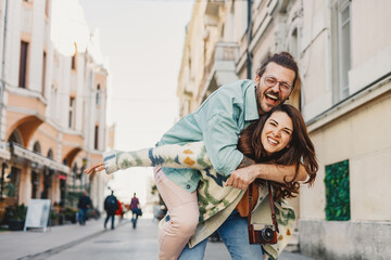 Playful fun hipster couple having piggyback ride on city street.