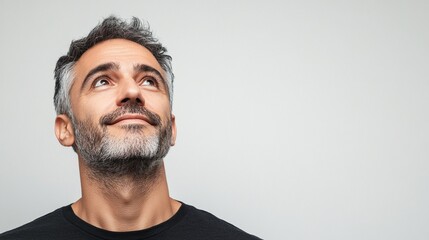 Obraz premium Mid-aged man looking up with curiosity, against a light background in close-up, expressive and thoughtful gaze