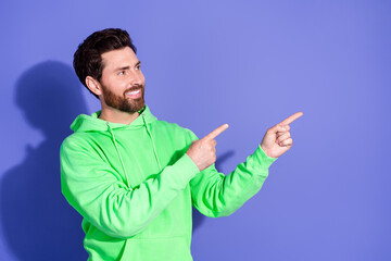 Photo portrait of brunet hair mature age funky man wearing neon green hoodie pointing fingers empty space promo cafe isolated on violet color background