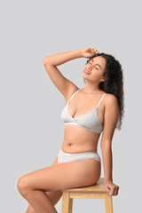 Naklejka premium Beautiful young happy African-American body positive woman sitting on chair against grey background