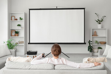 Woman sitting on sofa with projector screen in room, back view
