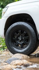 A white vehicle navigates an off-road trail, splashing through water and rocks. Close-up highlights include fog lights and a dark wheel hub, emphasizing its rugged features