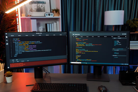 Programming code on computer two screens on desktop placing working desk showing intelligent website development coder system running data online information technology at neon light room. Infobahn.