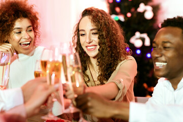 Multiracial Friends Celebrating New Year Together Clinking Glasses And Toasting Sitting At Table Indoors. Selective Focus