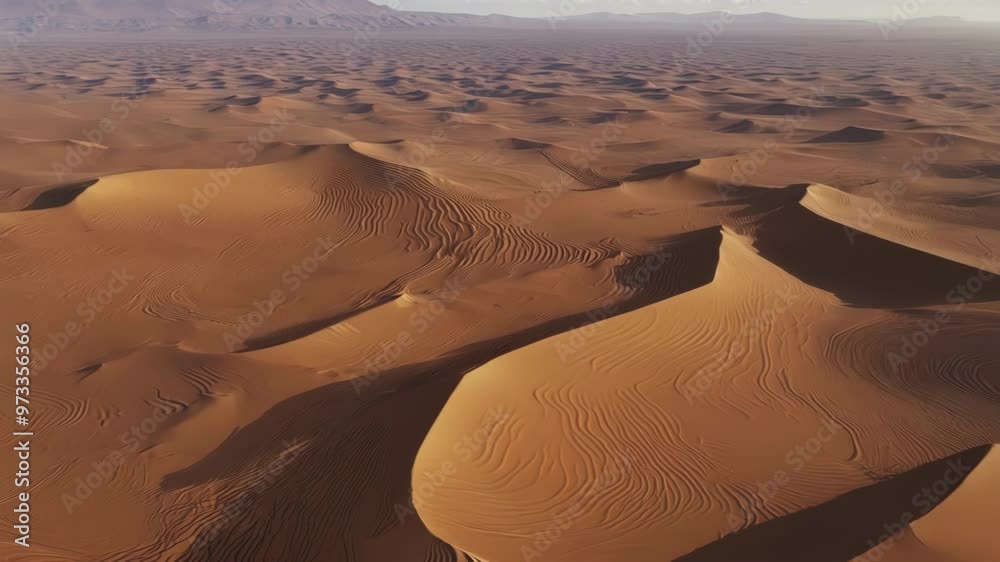 Poster Basking in warm sunlight. Wind blown sand dunes create a mesmerizing landscape stretching endlessly. With peaks. Valleys. And distant mountains adding to the scenic view of the vast