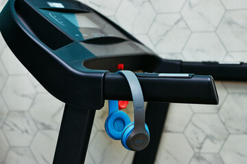 Modern treadmill with digital display for indoor running and fitness workouts and blue wireless headphone 