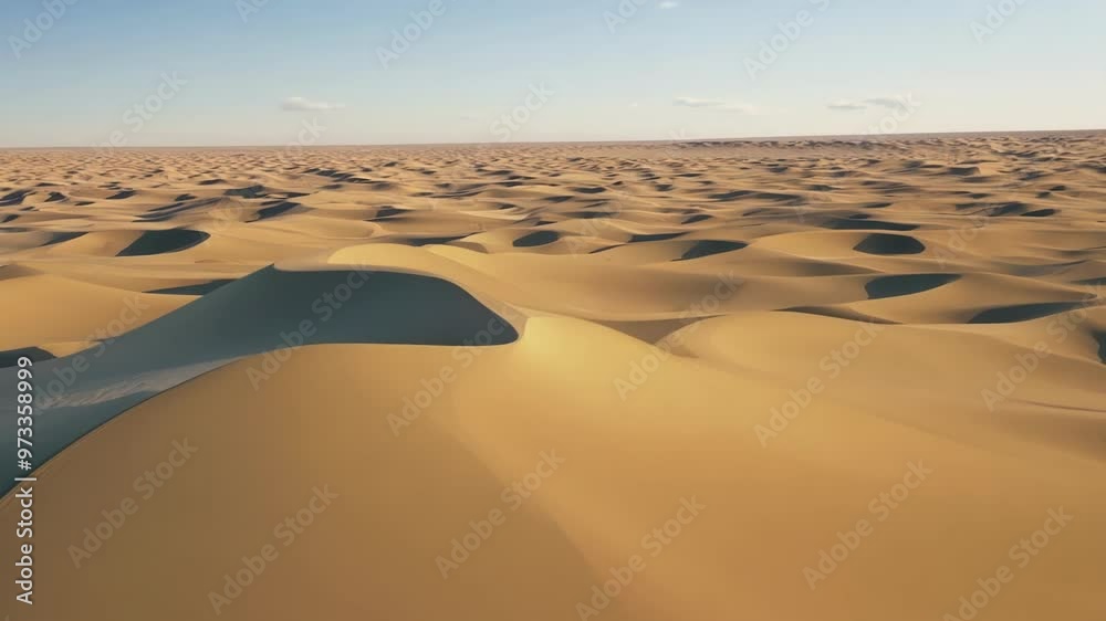 Poster Aerial view of a vast desert landscape with sand dunes bathed in warm sunlight, creating a mesmerizing pattern of light and shadow