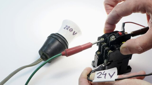 Hands wiring an electric contactor with a 24 volt coil to power a 220 volt bulb, demonstrating a basic electrical circuit