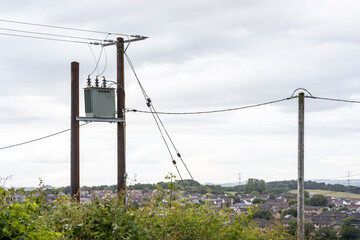 Fototapeta premium Electricity supply transformer and distribution power lines on wooden telegraph poles in rural Ayrshire Scotland