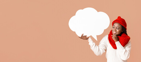 Pretty interested woman in winter hat holding communication bubble, touching her chin, beige studio background