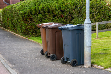 UK recycling wheelie bins brown grey lined up at kerbside storage area front garden