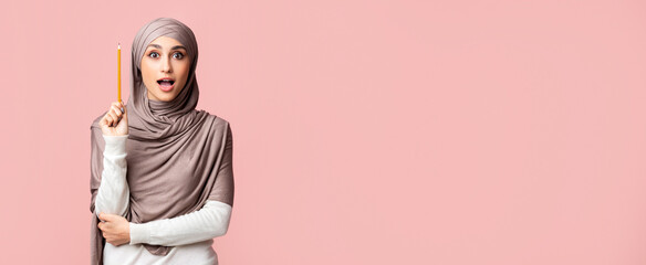 New Idea. Inspired muslim girl in hijab holding pencil in raised arm, opened mouth in exitement, posing over pink background with free space