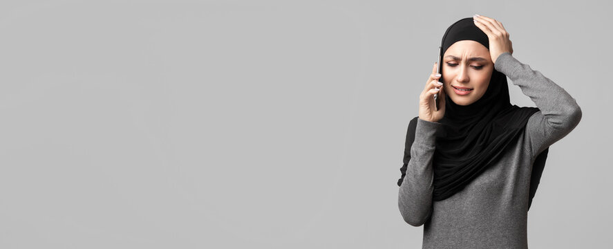 Desperate crying muslim woman in hijab talking on cellphone, calling somebody for help and support, having problems, grey background with empty space