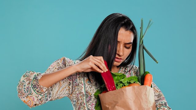 Upset woman frowning after forgetting to buy everything, looking inside paper bag with vegetables. Conscious living person sulking after realizing some groceries are missing, camera B