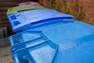 Plastic Waste Recycling Wheelie Bins lined up and secured in a UK garden storage area beside house...