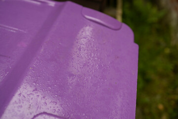 Purple lid on waste recycling wheelie bin close up in garden storage area for glass bottles and jars