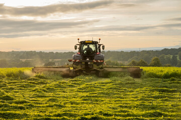 Farm tractor and mower cutting hay field at sunset in Scottish farmland © Tosh Lubek