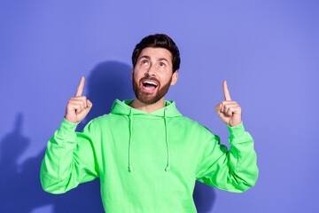 Photo of handsome mature age funky man wearing bright green hoodie pointing fingers up enjoying empty space isolated on violet color background