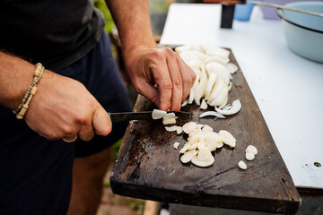 A man is skillfully cutting onions on a wooden cutting board very carefully