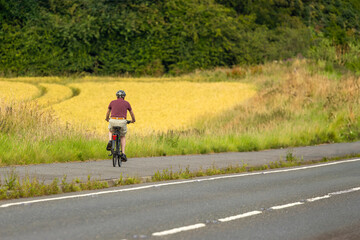 Obraz premium Senior cyclist on cycleway beside road and field of ripening barley