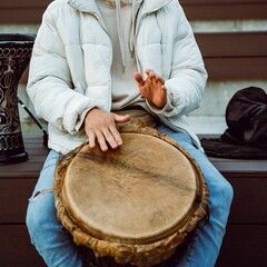 A person is playing a traditional drum in an outdoor setting, creating a vibrant atmosphere filled...