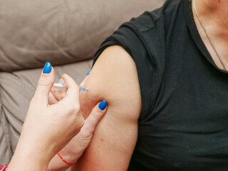 A man is getting a shot in his arm by a woman with blue nail polish, couch in the background. Amateur non professional Injection of medicine or vitamins due to poverty. Drug use and vaccination