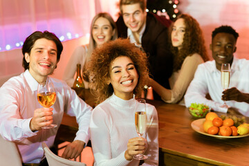Cheers, Merry Christmas. Friends Holding Glasses Toasting Celebrating Xmas Sitting At Table Indoors, Smiling To Camera.