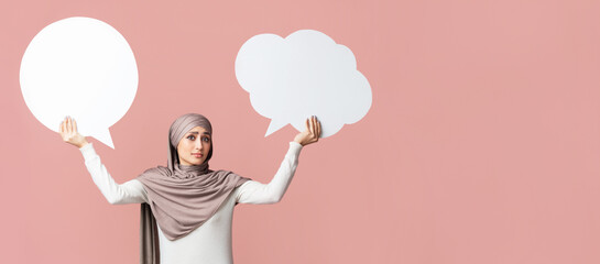 Difficult choice. Muslim girl in hijab holding two empty speech bubbles over pink background, free space