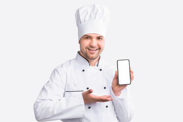 Restaurant Chef Showing Cellphone With Empty Screen Recommending Food Delivery Service Standing On White Studio Background. Panorama