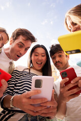 Vertical. Diverse group young people in circle staring in surprise at cell phone together outdoor....