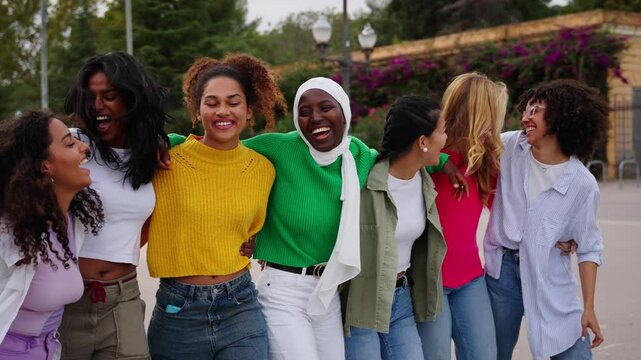 Lively diverse group only young women friends strolling embracing in line laughing in spring city park. Excited urban nice generation z female community enjoying together walking hugging outdoors