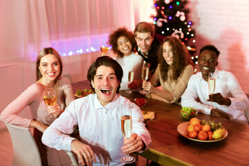 Cheers. Happy Group Of Millennial Friends Holding Glasses Smiling At Camera Sitting At Table Having Christmas Home Party Indoor