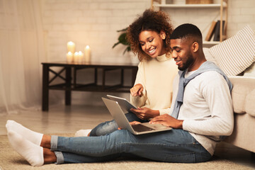 Happy african-american spouses browsing internet on gadgets, using laptop anf tablet at home, copy...