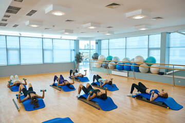 Health group performs strength exercises with dumbbells, lying on special platforms