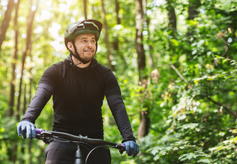 Smiling professional cyclist looking around while cycling in forest, copy space