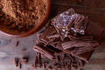 Top view of chocolate pieces and cocoa powder on wooden background.