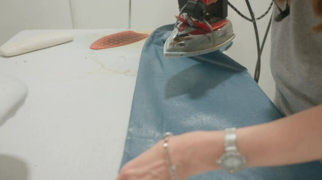 Close-up view of a female worker ironing clothes. Dry cleaner, laundry, industrial factory, clothing production. Professional steaming of clothes. High quality 4k footage