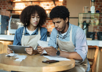 Problems in small business during covid-19 lockdown. Sad millennial african american couple owners in aprons work with accounts, and solve debt problems bookkeeping in cafe, empty space