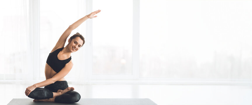 A woman performs a side stretch in a modern yoga studio filled with natural light, panorama with copy space