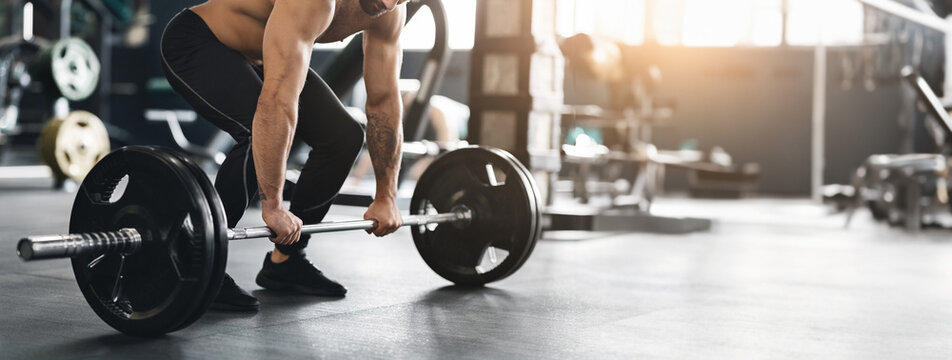 Hard strength workout. Muscular powerlifter lifting heavy barbell from gym floor, empty space, cropped