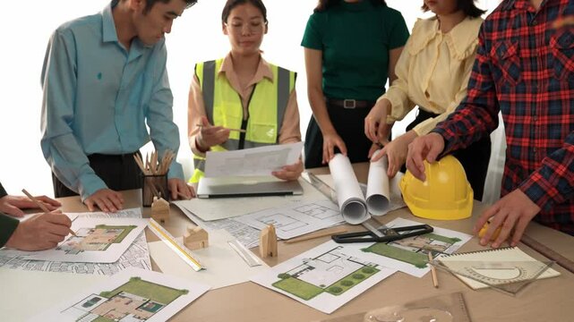 Smart architect and safety engineer discussion about building blueprint on table with architectural document, measurement tools and wooden block scatter around at modern office. Closeup. Delineation.