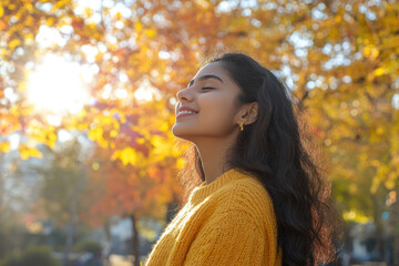 Indian woman wearing yellow knitted sweatshirt in autumn park at sunny day