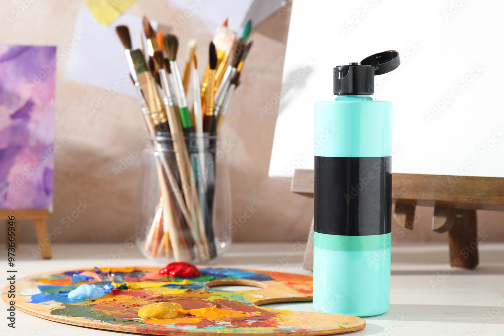 Wall mural Turquoise acrylic paint in bottle, small easels, palette and brushes on wooden table indoors