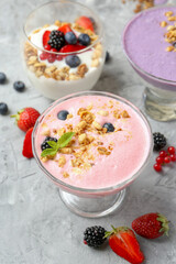 Different tasty yogurts with fresh berries and granola in glass dessert bowls on gray textured table, closeup