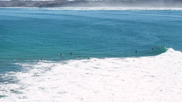 Surfers waiting for waves on a beach in Raglan, New Zealand