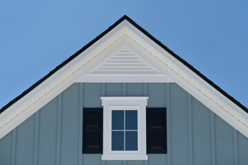 White frame attic window vent on blue siding, gable, corbel, louver on a new construction luxury American single family home in the East Coast USA with blue sky background   © tamas